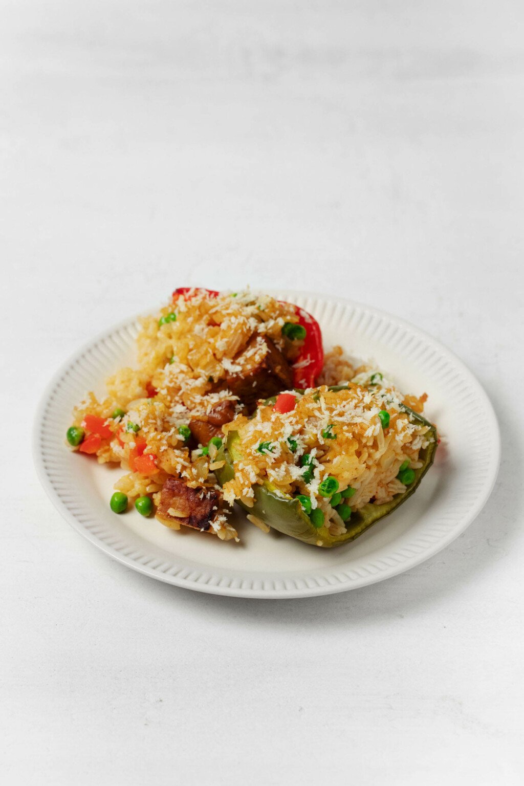 Two bell peppers are stuffed with a whole grain mixture. They rest on a round, rimmed white ceramic plate.