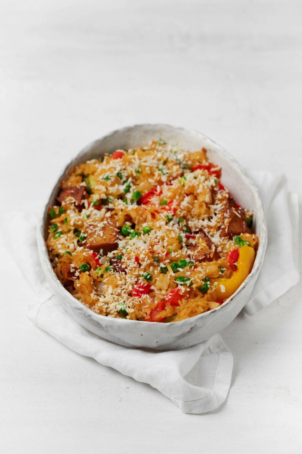 An oval-shaped, white baking dish has been filled with vegan stuffed peppers and topped with dairy-free, grated cheese.