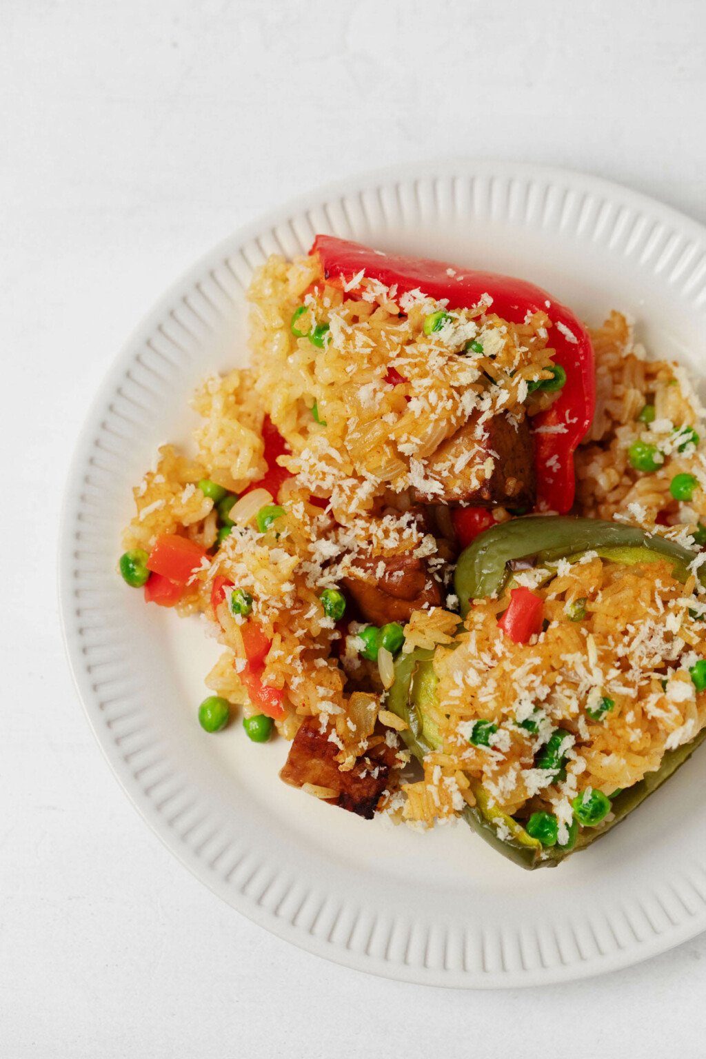 An overhead image of stuffed pepper halves, made with rice and tempeh, which are resting on a round, white plate.