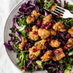 A shallow plate holds a festive, colorful salad of spiced, roasted cauliflower, raw kale, and pomegranate seeds.