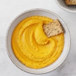 An image of roasted carrot hummus with a seedy cracker.