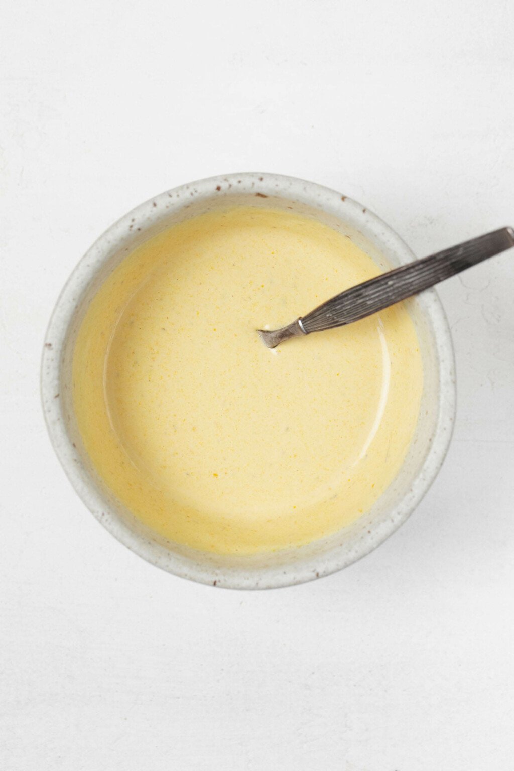 An overhead image of a small, white bowl filled with a creamy, golden dressing.