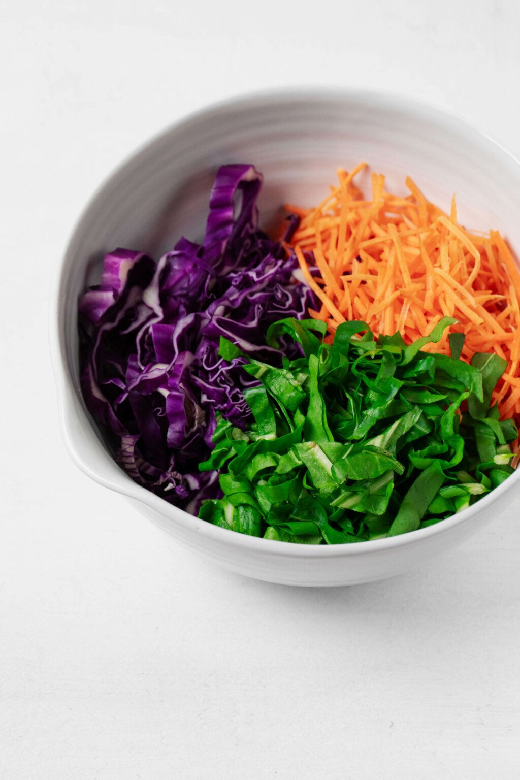 A large mixing bowl is filled with cabbage, carrots, and sliced collard greens.