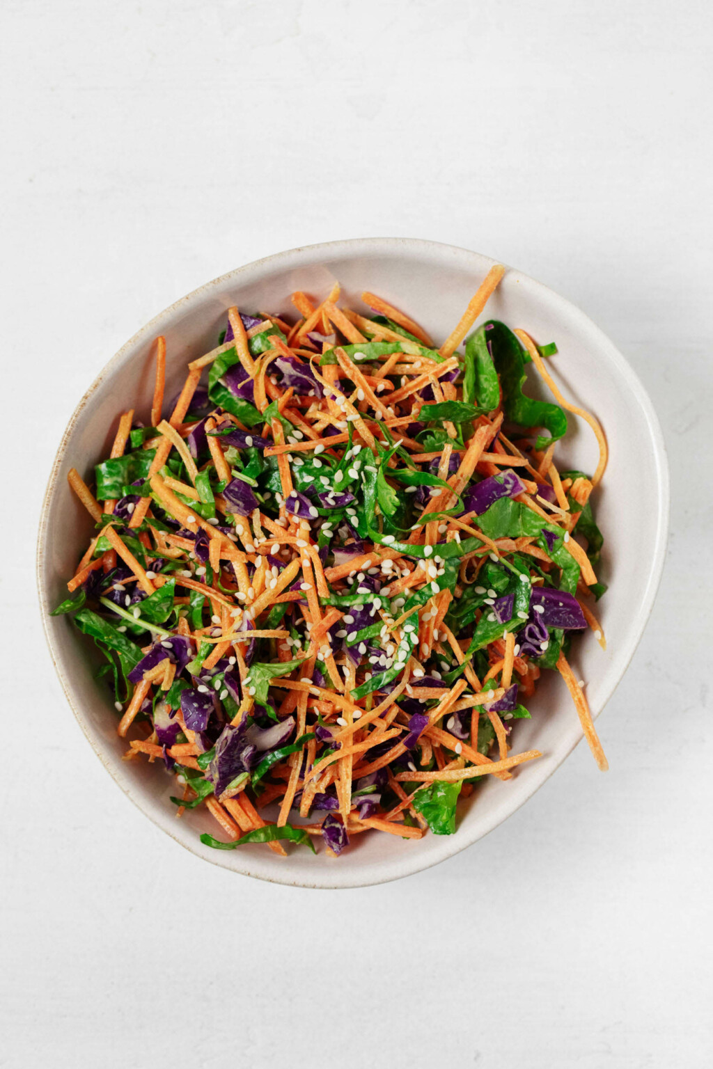 An overhead image of a bowl of colorful turmeric slaw, prepared with mixed vegetables and garnished with sesame seeds.