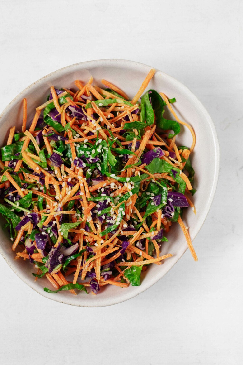 An overhead image of a bowl of colorful turmeric slaw, prepared with mixed vegetables and garnished with sesame seeds.