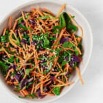 An overhead image of a bowl of colorful turmeric slaw, prepared with mixed vegetables and garnished with sesame seeds.