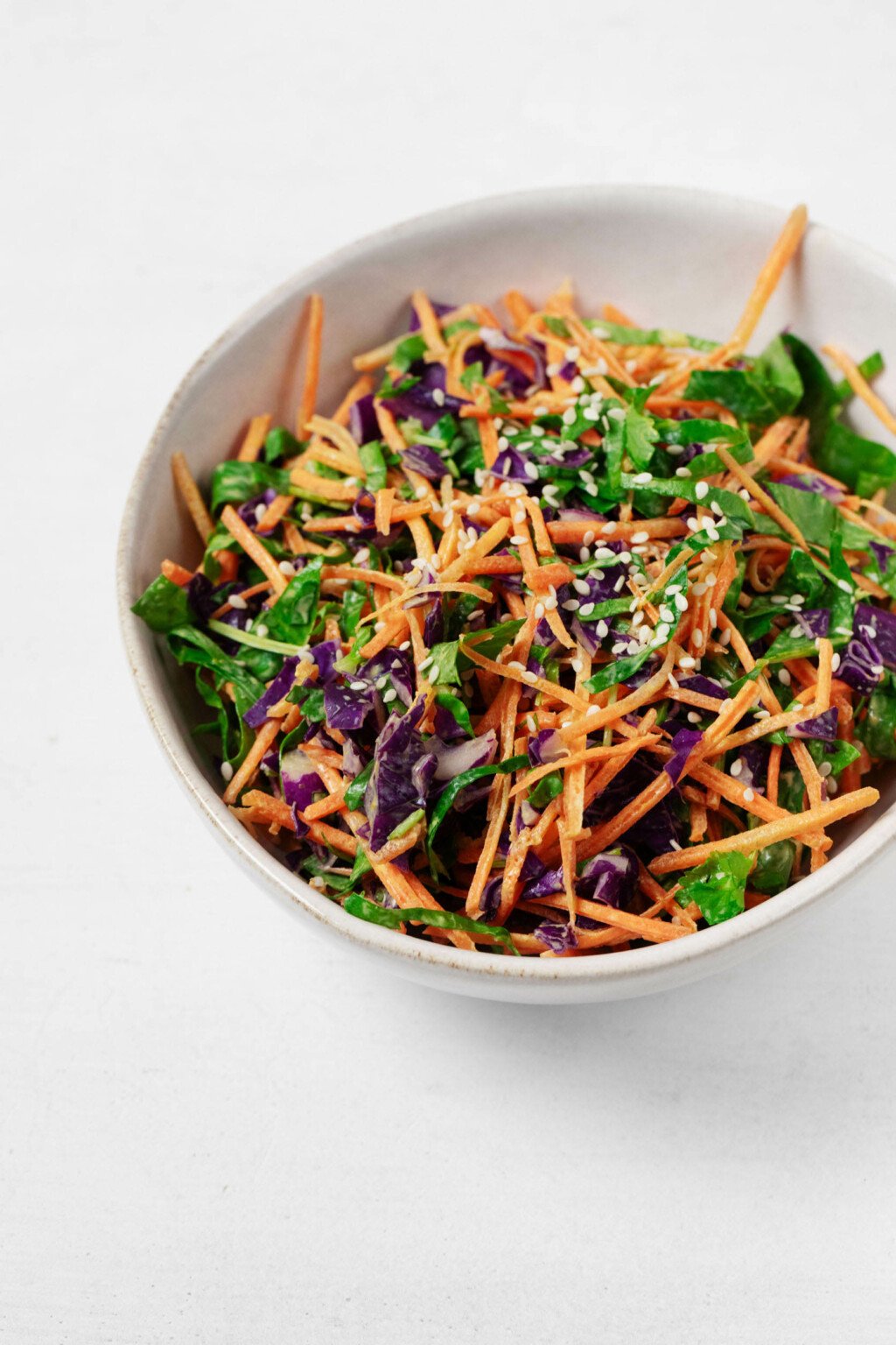 An overhead image of a bowl of colorful turmeric slaw, prepared with mixed vegetables and garnished with sesame seeds.