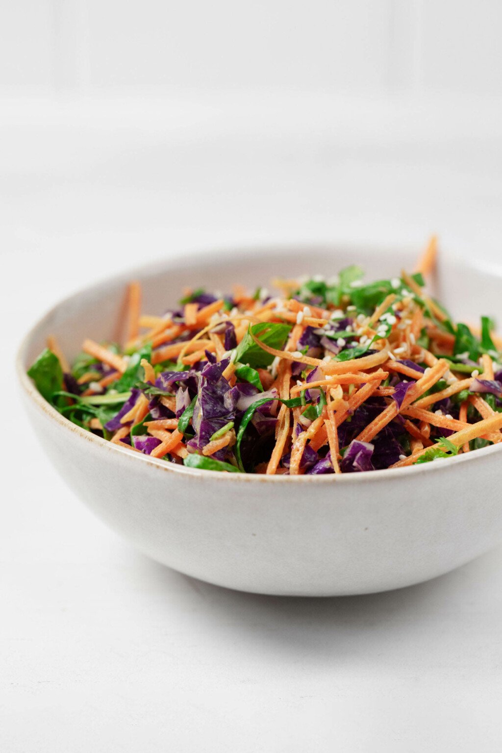 An overhead image of a bowl of colorful vegetable slaw, prepared with a creamy turmeric dressing and garnished with sesame seeds.