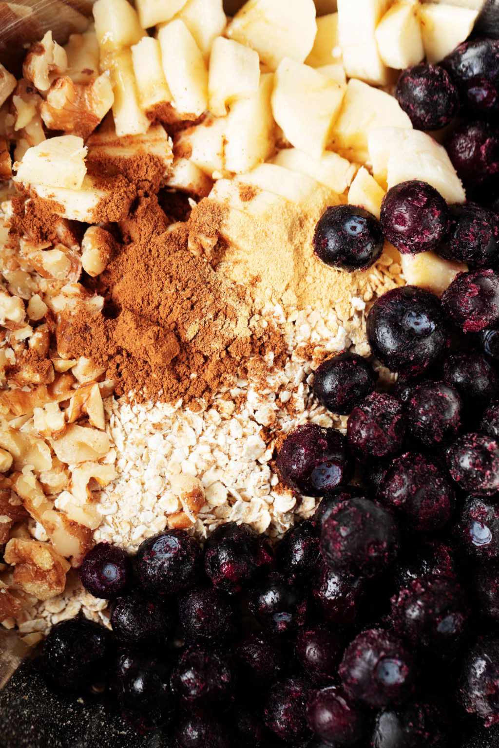 A zoomed in, overhead image of fruit, nuts, oats, and spices in a mixing bowl.