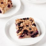 Three small white plates are holding a vegan oat bake with blueberries and banana.