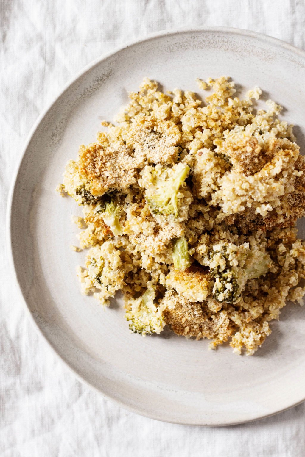 A cheesy vegan quinoa bake has been portioned onto a light gray ceramic plate. 