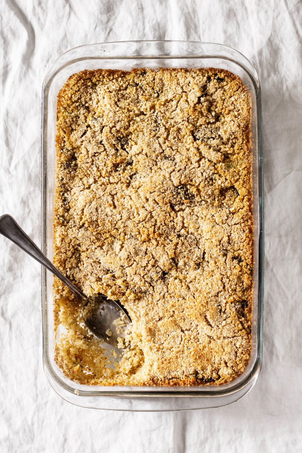 A glass casserole dish is filled with baked whole grains and broccoli. It's being portioned with a silver spoon.