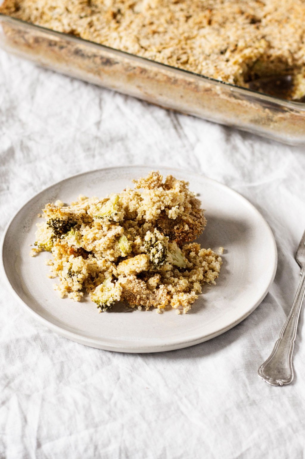 A quinoa and broccoli baked casserole has been portioned onto a white plate. It rests on a gray linen tablecloth.
