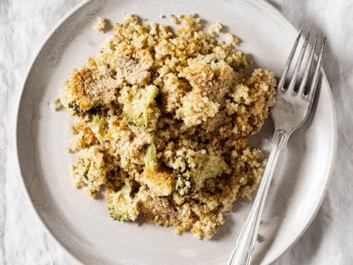 A ceramic plate rests on a gray linen cloth. It holds a cheesy vegan quinoa bake.