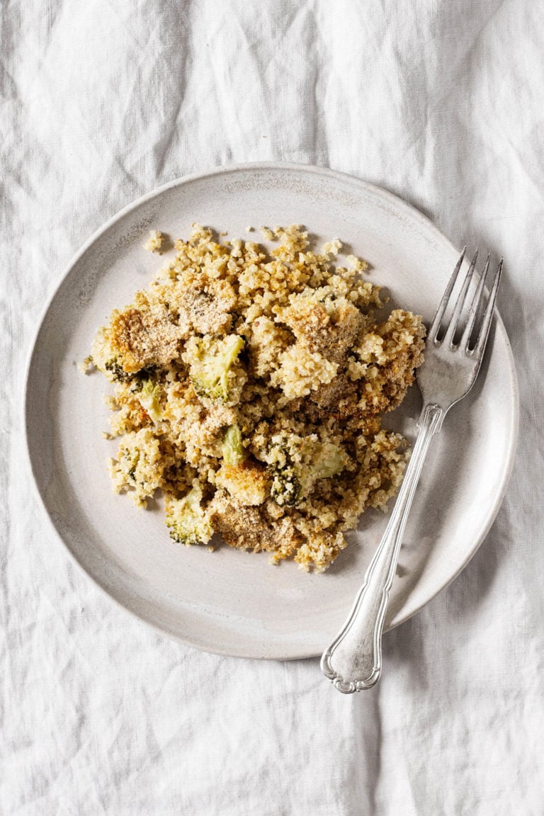 A ceramic plate rests on a gray linen cloth. It holds a cheesy vegan quinoa bake.