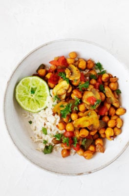 A white, rimmed bowl has been filled with a bed of cooked rice and a scrambled chickpea mixture, then sprinkled with bright green parsley.