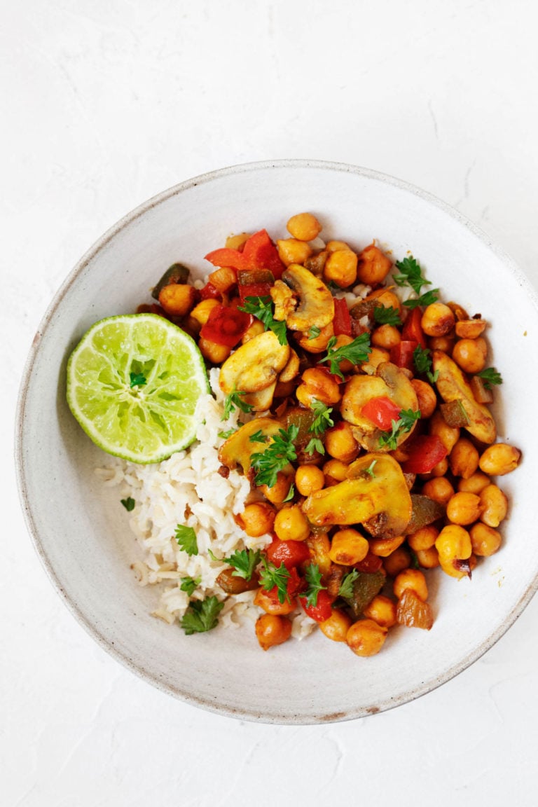 A white, rimmed bowl has been filled with a bed of cooked rice and a scrambled chickpea mixture, then sprinkled with bright green parsley.