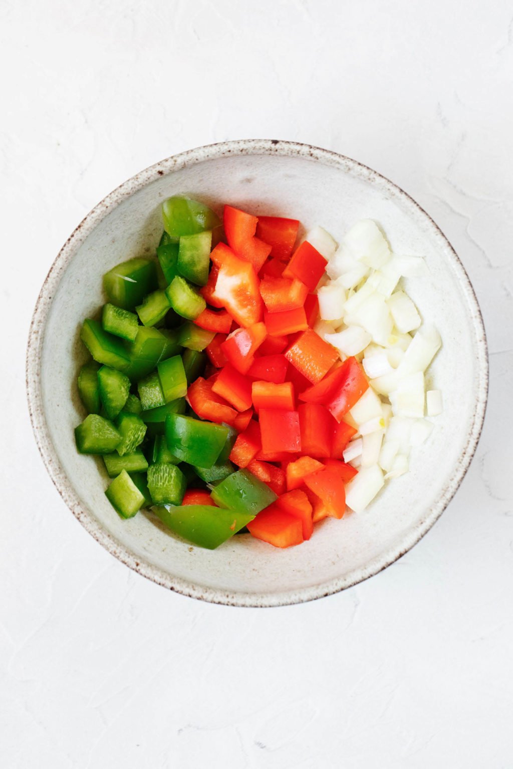 A white bowl with a light gray rim holds chopped onion and peppers.