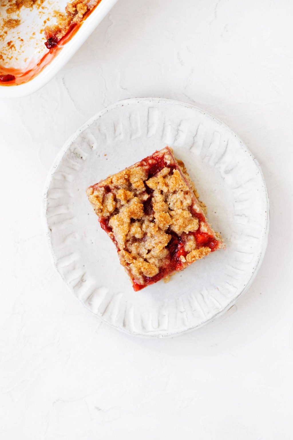 A small white dessert plate has been topped with a rustic, plant-based fruit dessert that's cut into a square shape.