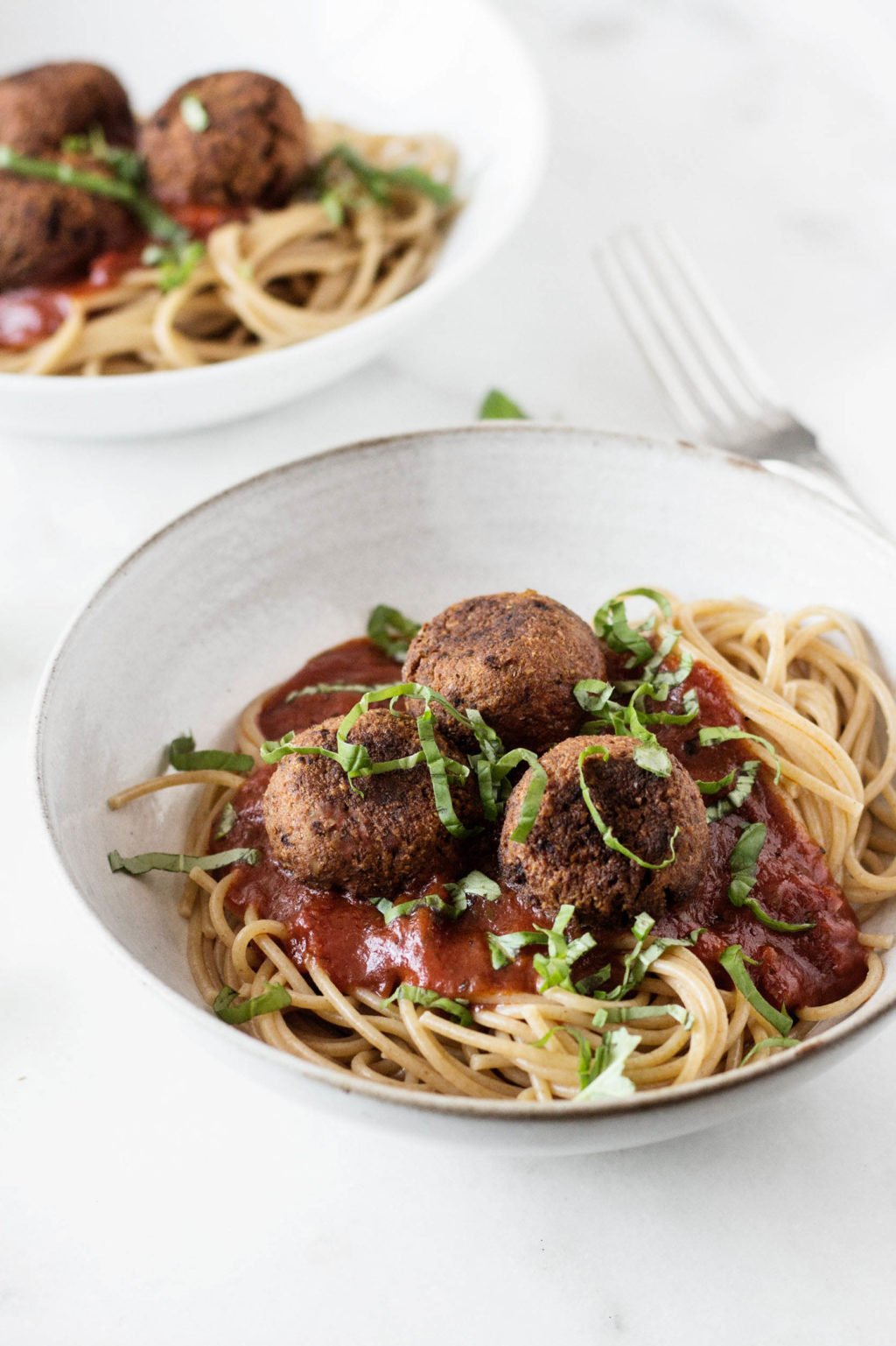 A white bowl has been filled with a mix of spaghetti & white bean balls, along with marinara sauce. It's topped with fresh, sliced basil.
