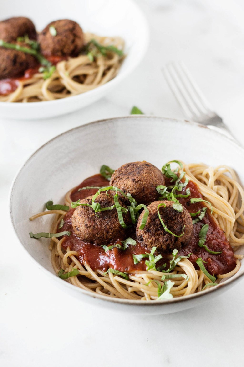 A white bowl has been filled with a mix of spaghetti & white bean balls, along with marinara sauce. It's topped with fresh, sliced basil.