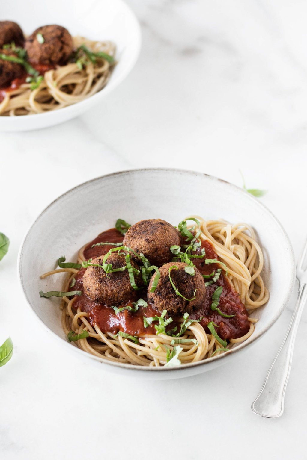 Two bowls have been filled with pasta and a vegetarian protein. They're topped with marinara sauce and rest on a white surface.