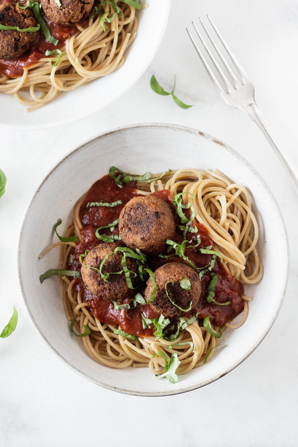 An overhead image of a round, white bowl of vegan spaghetti & white bean balls, smothered in marinara sauce.