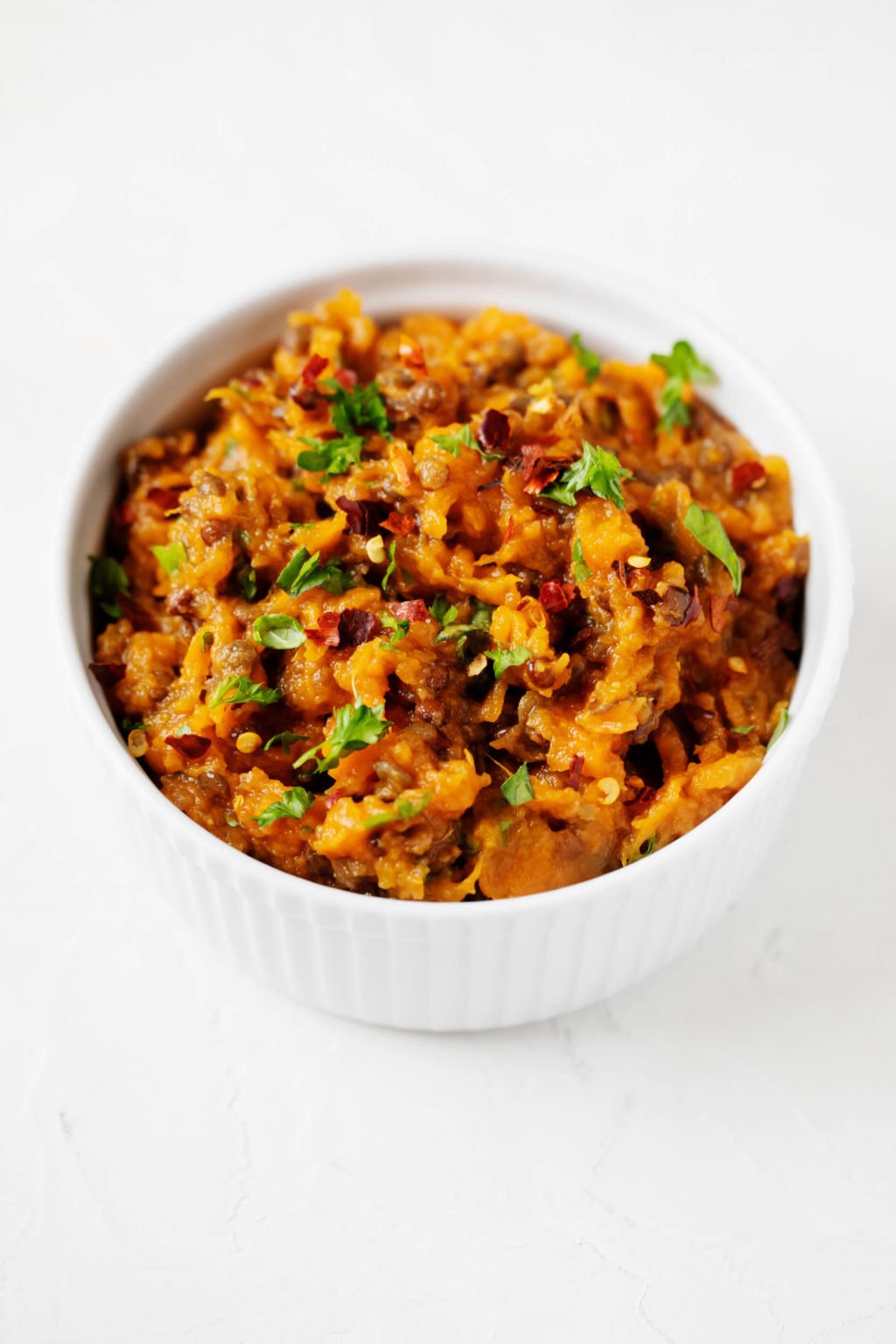 A while ramekin has been filled with a bright orange, plant-based spread and a garnish of parsley.