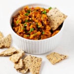 A white ramekin has been filled with a lentil sweet potato salad and is accompanied by crackers.