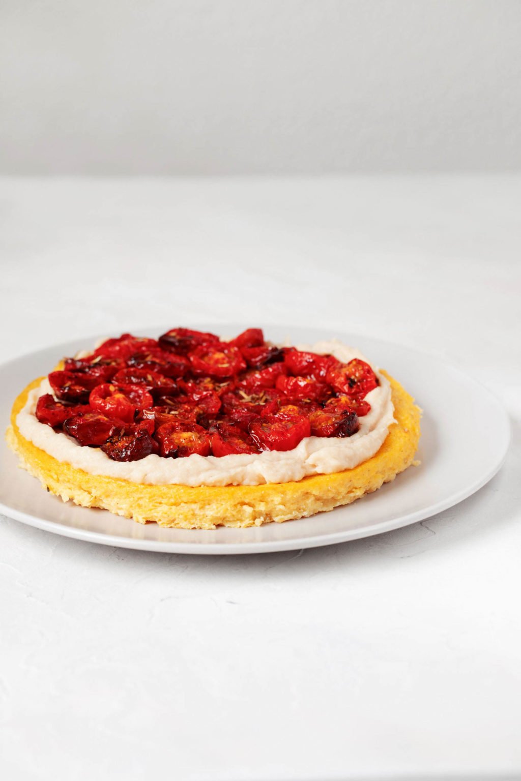 A wide-rimmed, round white plate is holding a summer appetizer with fresh tomatoes. It rests on a white surface.
