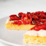 An angled image of a polenta and cherry tomato tart, which is topped with a white bean spread.
