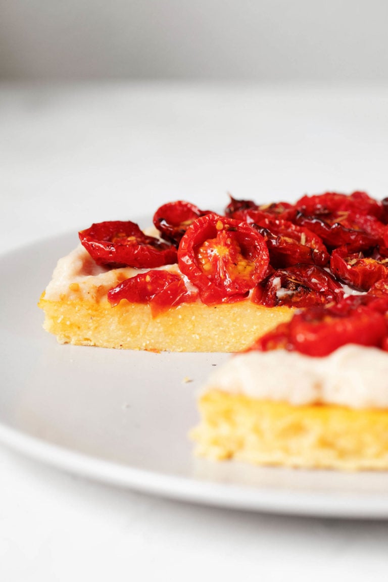 An angled image of a polenta and cherry tomato tart, which is topped with a white bean spread.