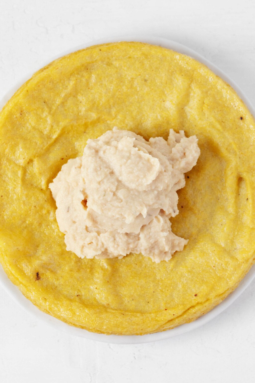 A white bean dip has been placed on top of a round of baked, firm polenta.