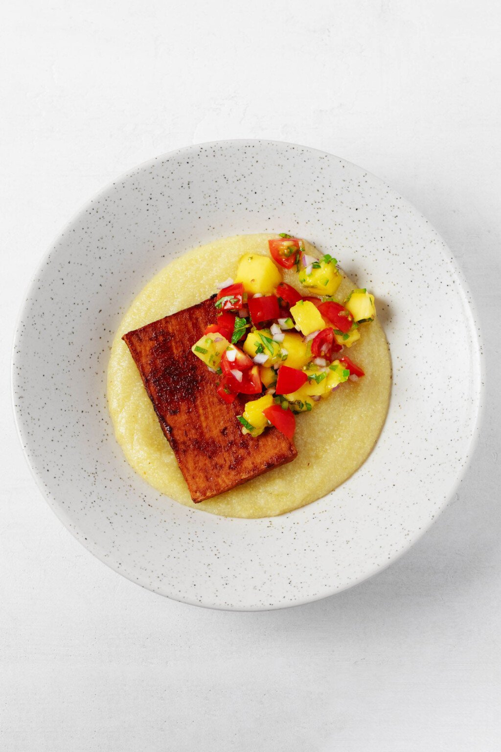 An overhead image of a bowl of soft polenta, which has been topped with BBQ tofu and fresh salsa.