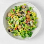 An overhead image of a colorful corn, black bean, and tempeh salad with mixed vegetables and a creamy dressing. It is served in a large white bowl.