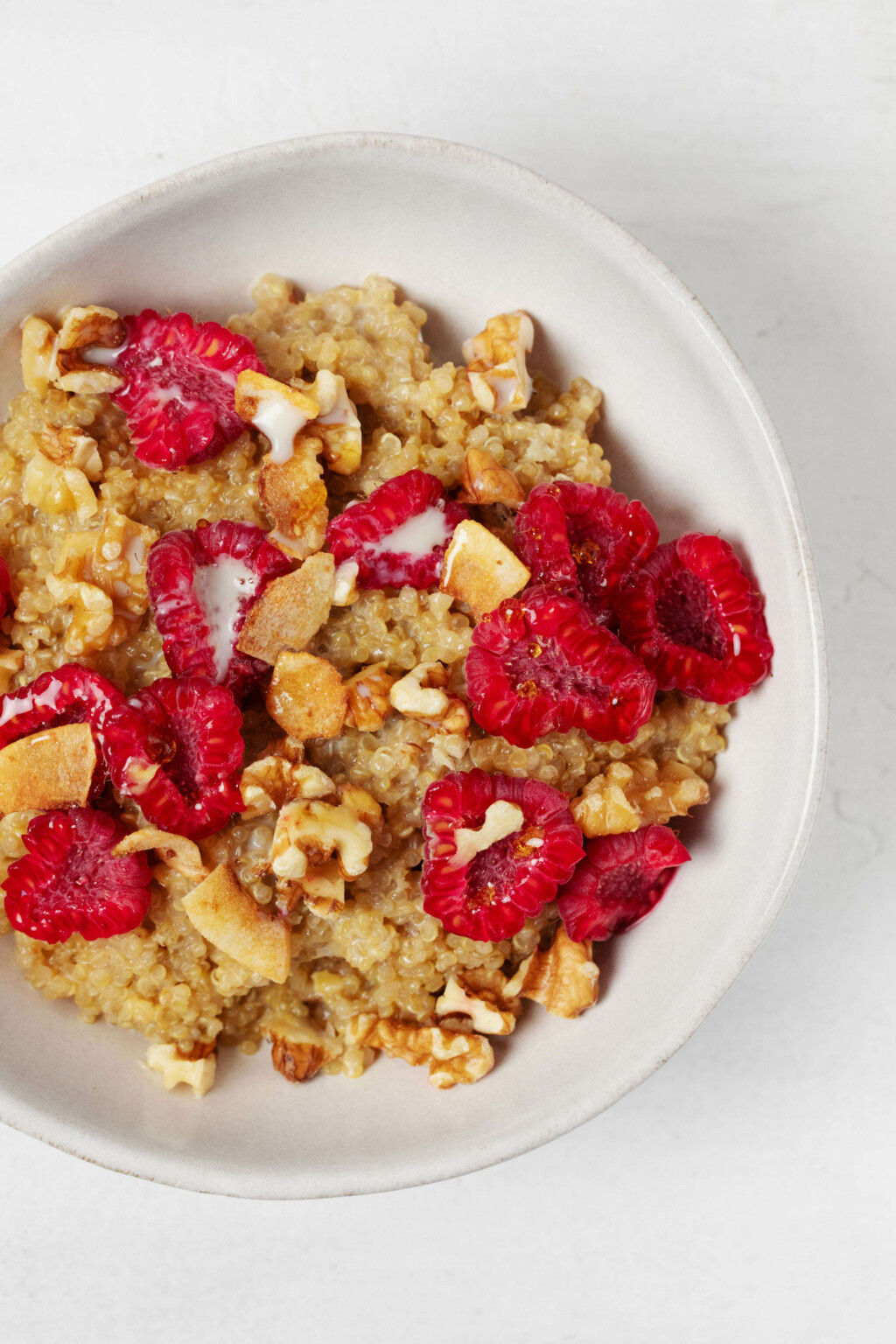 An overhead image of a quinoa porridge, which has been topped with raspberries, nuts, and coconut flakes.