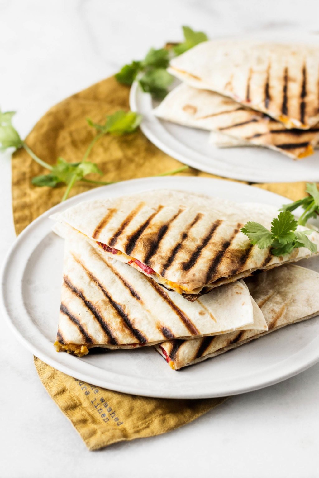 A stack of quesadillas has been prepared with plant-based ingredients. It's resting on a white plate and rust colored napkin.