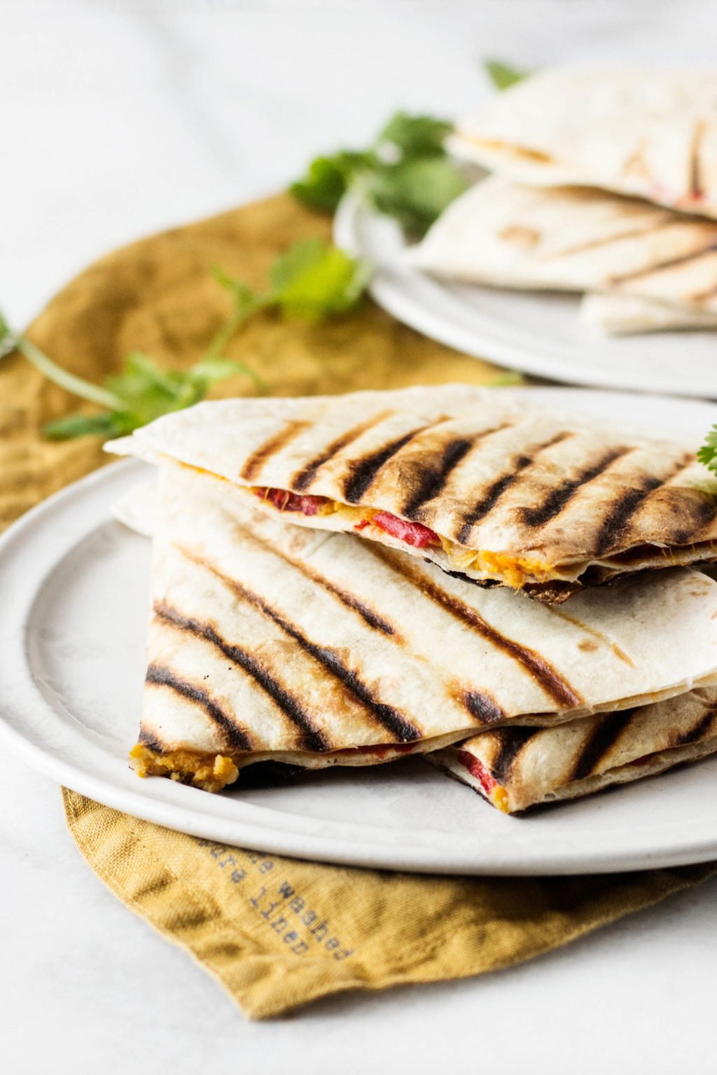 An angled photograph of grilled wraps, which have been made with roasted peppers and root vegetables. They're served on a plate, with a rust colored napkin nearby.