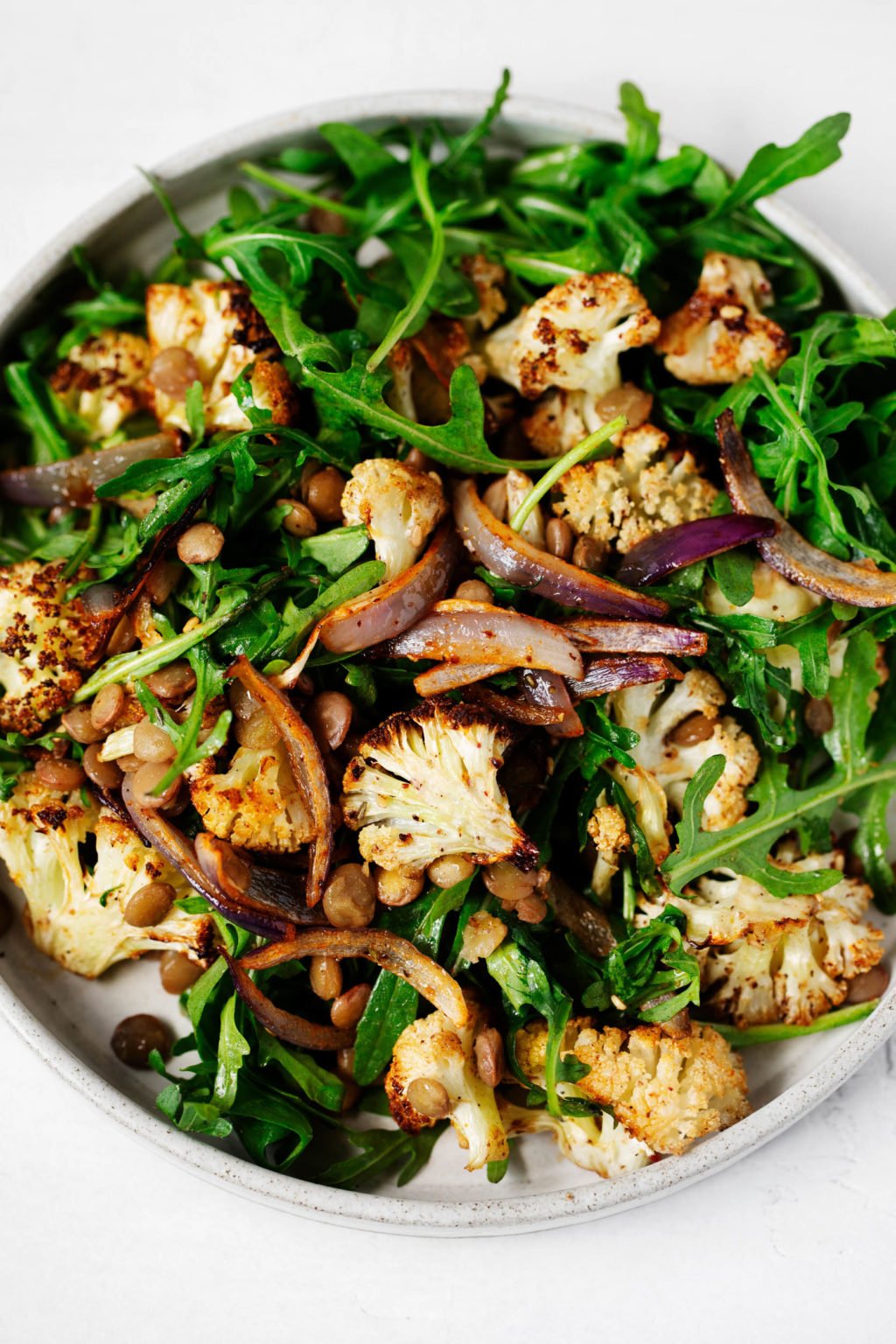 A zoomed in, birds eye photograph of a za'atar roasted cauliflower salad, which rests on a white ceramic plate.