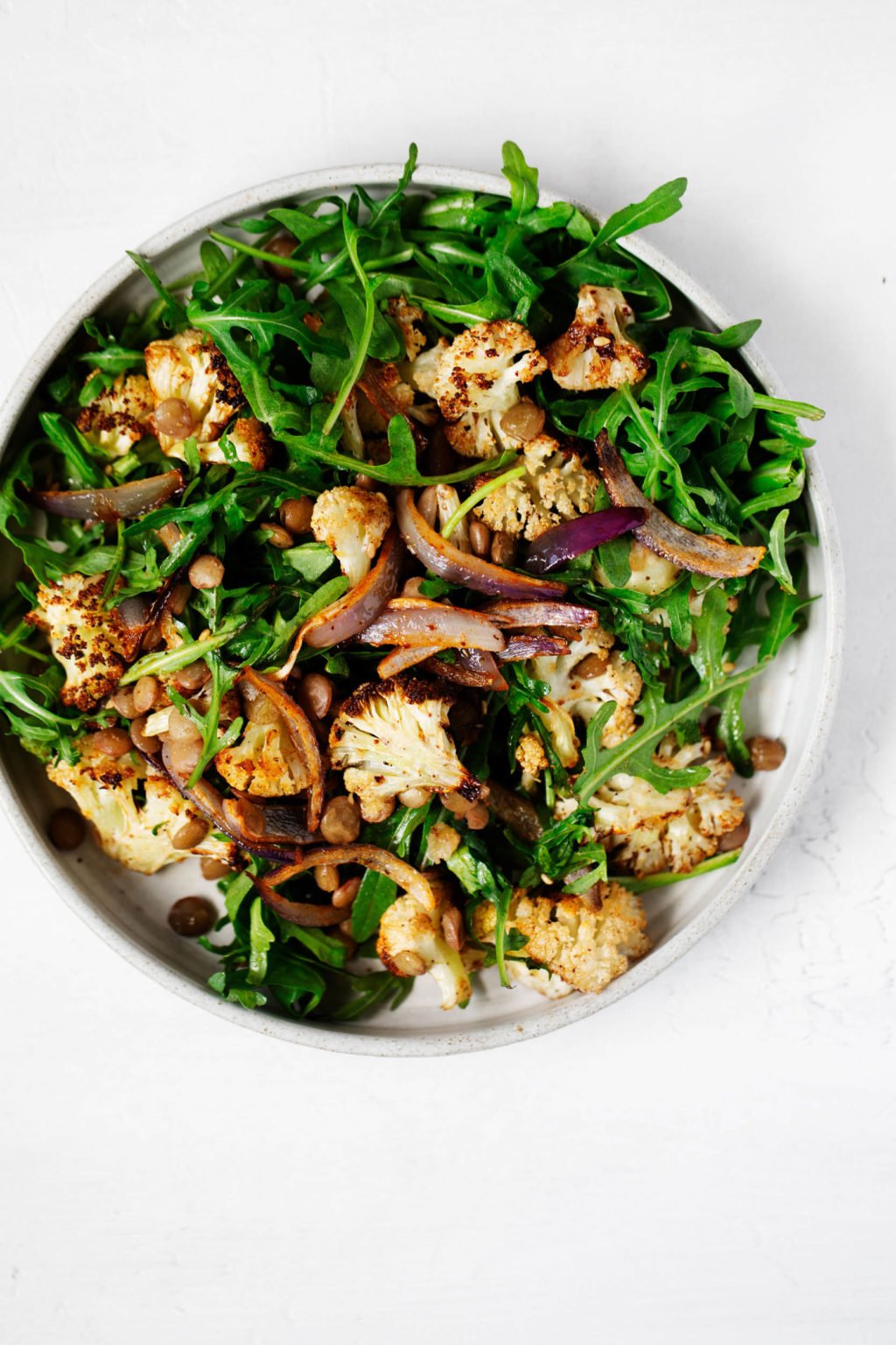 A white plate has been covered in a hearty, wintery salad with roasted vegetables and cooked lentils.