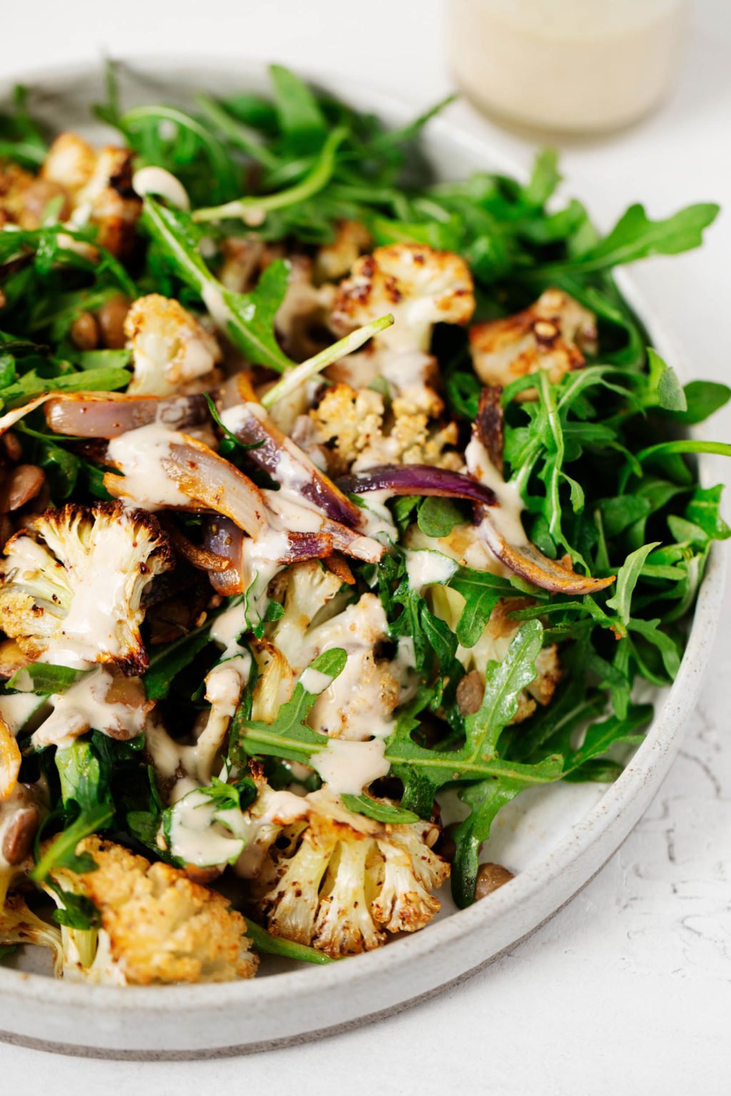 A white plate has been covered with a vibrant salad of za'atar roasted cauliflower, red onion, lentils and greens.