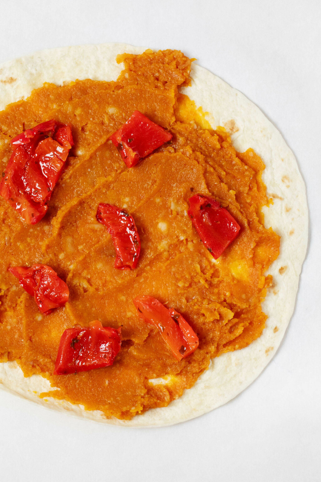 An overhead image of a round tortilla, which is filled with mashed sweet potato and pieces of roasted red pepper.