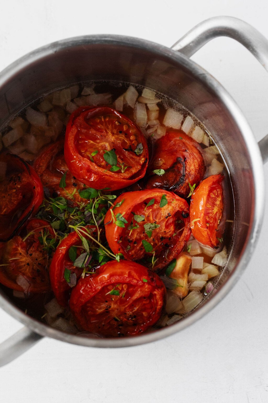 Roasted tomatoes are pictured in a metal pot with sautéed onion. 