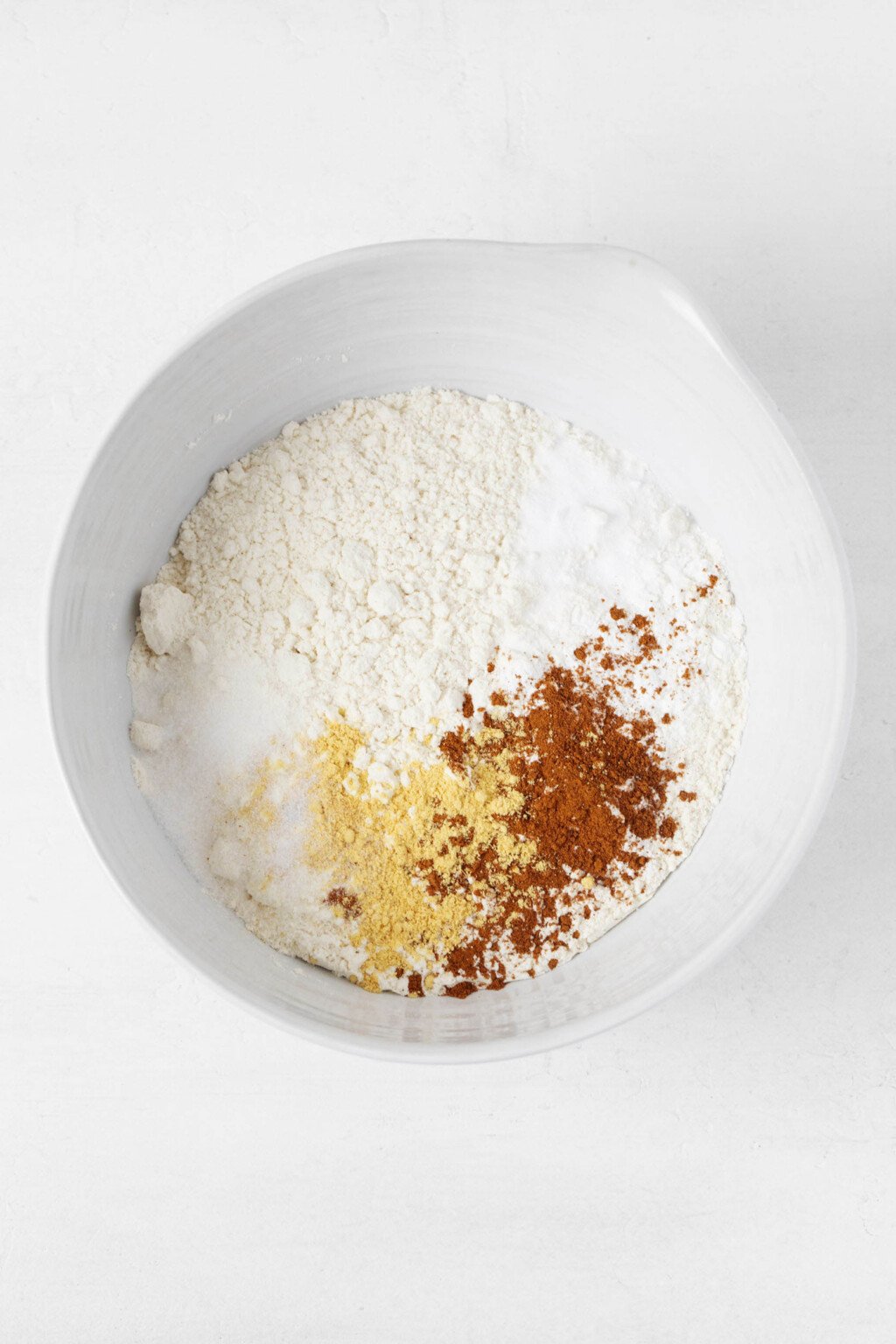Flour and spices are pictured in a large, white mixing bowl.