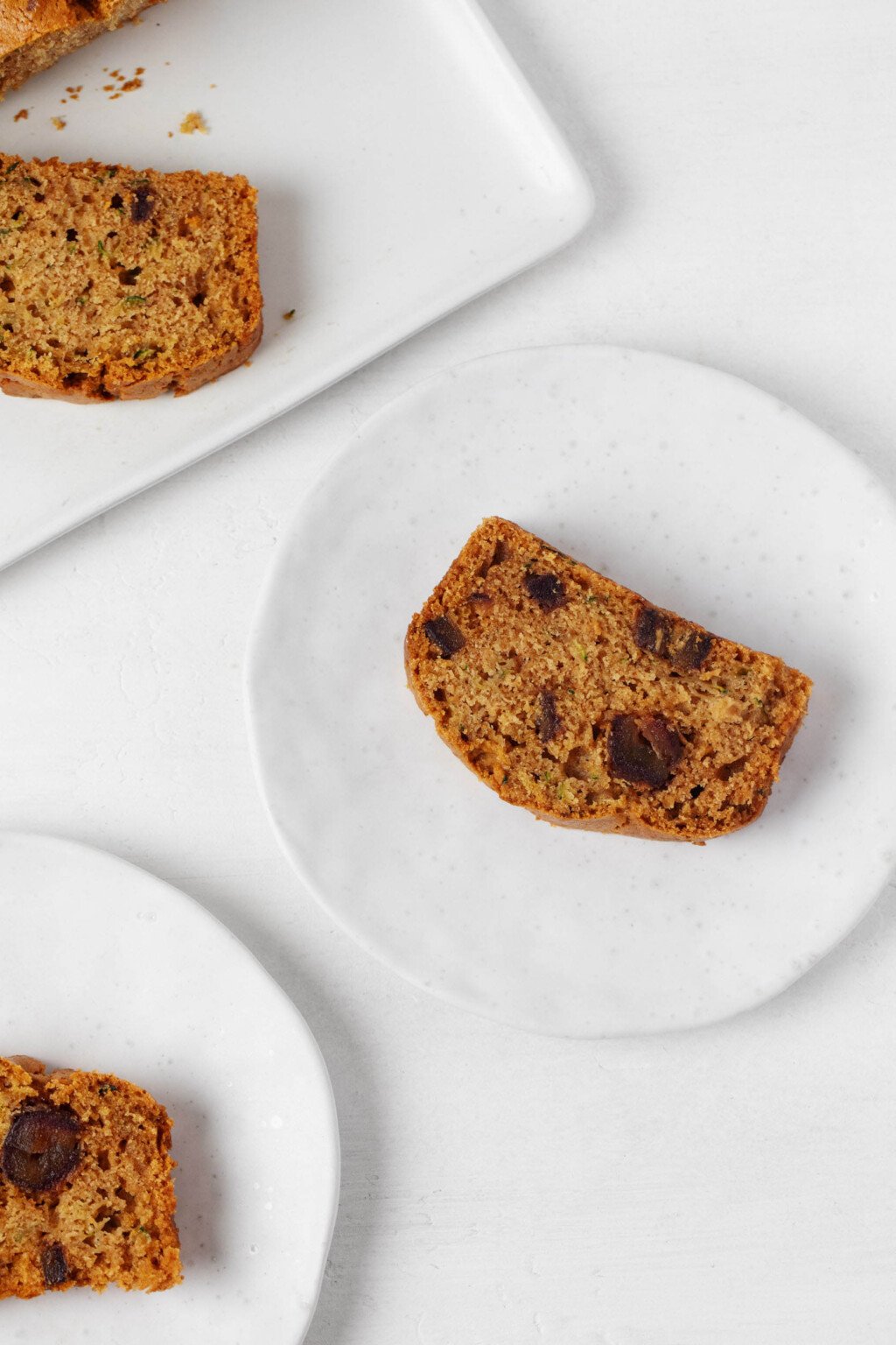 An overhead image of a moist slice of zucchini date bread, arranged on a small, round white plate.