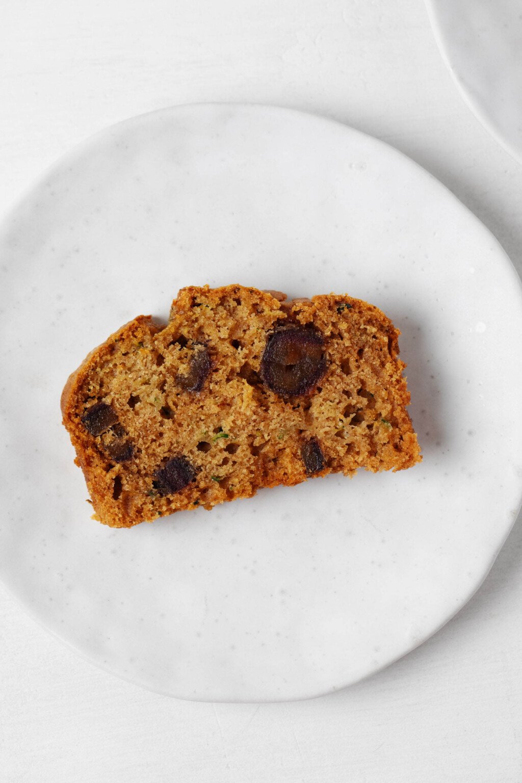 An overhead image of a moist slice of zucchini date bread, arranged on a small, round white plate.