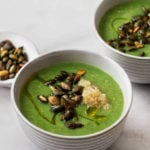 Two bowls of vegan cream of broccoli and quinoa soup, topped with toasted pepitas and a scoop of cooked quinoa.