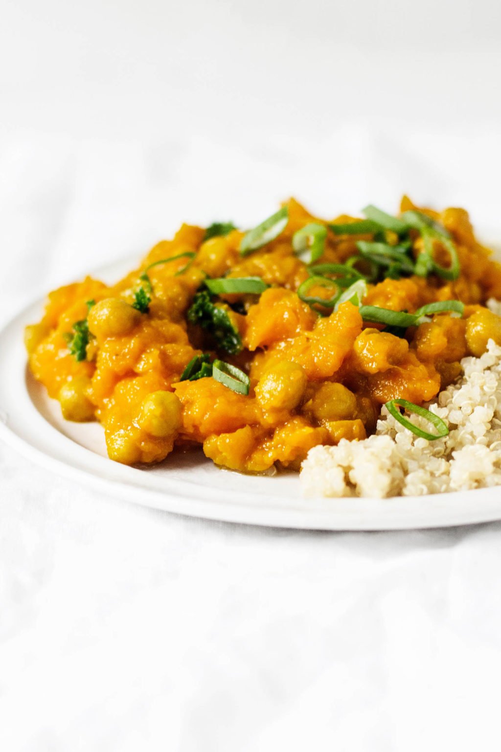 Curried butternut squash, golden raisins, and chickpeas make for a hearty and delicious winter meal. They're served with chopped green onions and cooked quinoa.