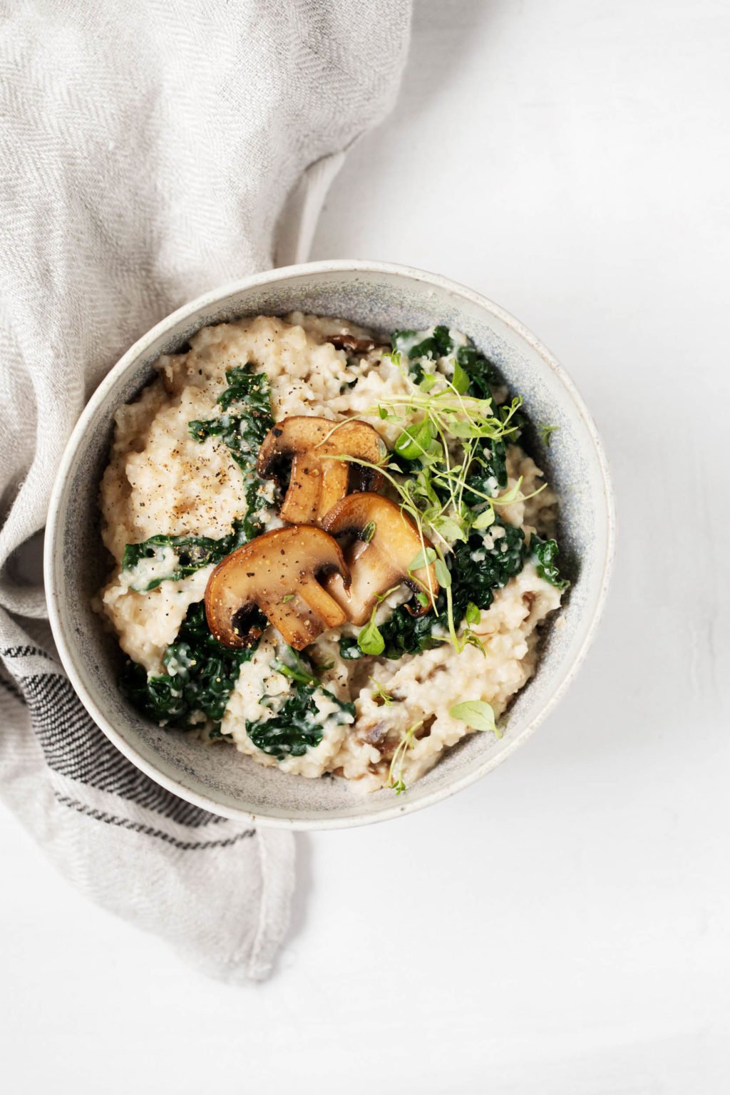 A small bowl of plant-based, savory oatmeal with mushrooms and greens, accompanied by a cloth napkin.