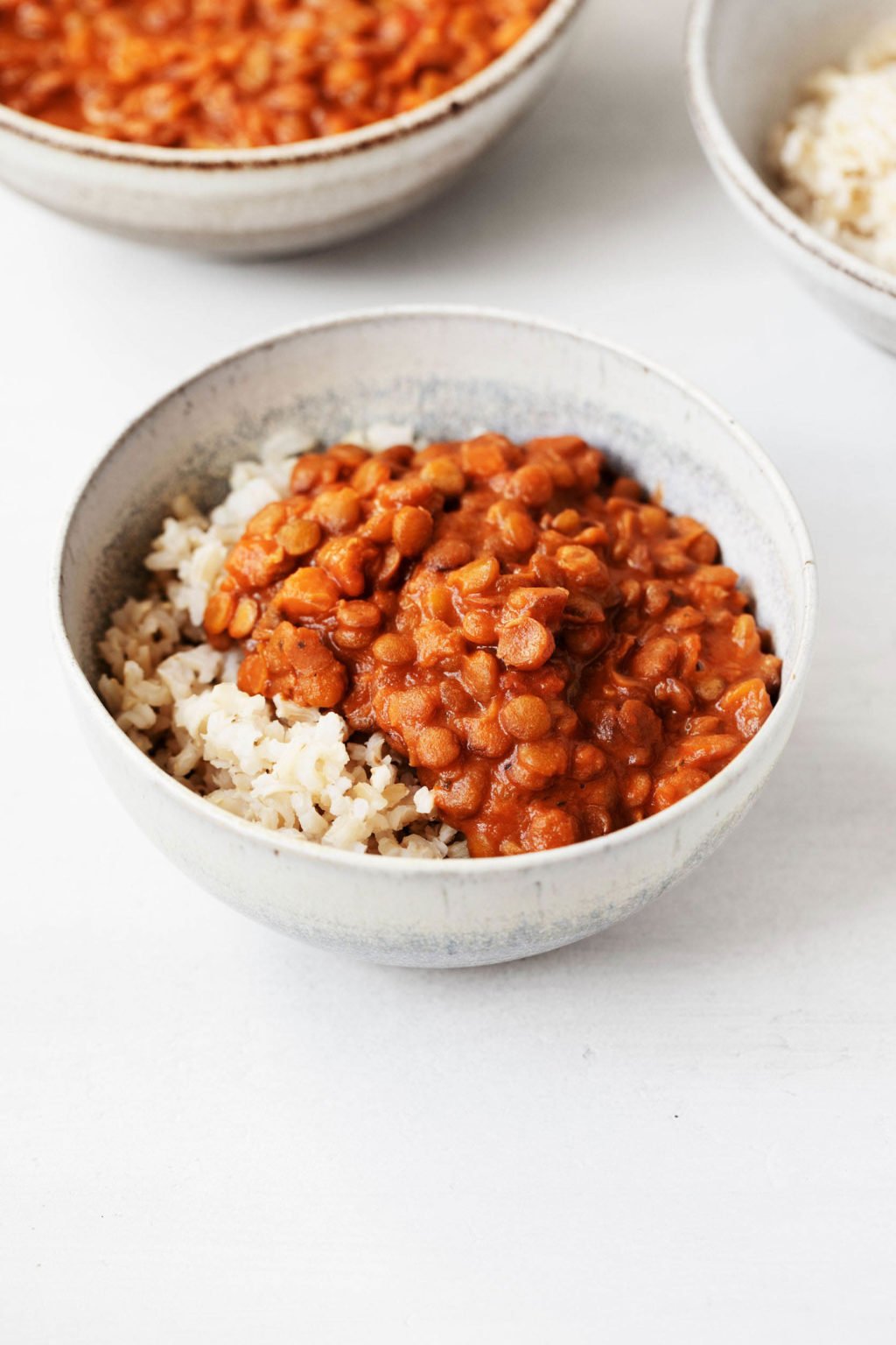 Two white, ceramic bowls hold dishes of masala spiced lentils and cooked brown rice.